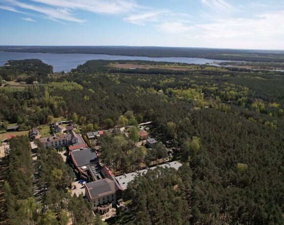 Hotel nad jeziorem wśród sosnowego lasu, taras i panele słoneczne na dachu, rozległy widok na wodę i wyspy