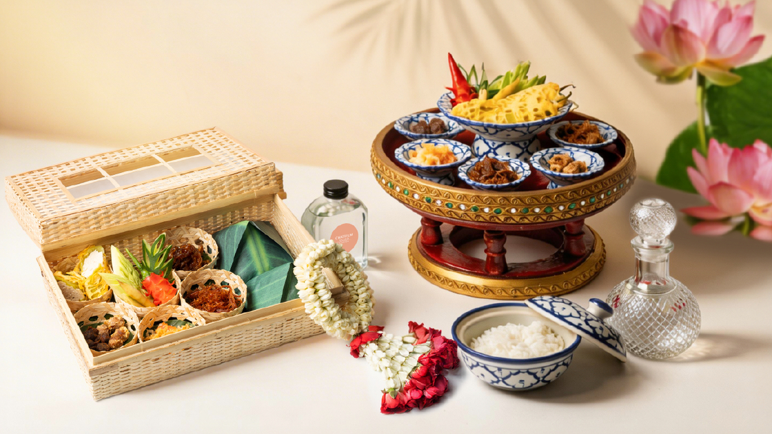 Traditional Thai welcome set with woven basket of small condiments, ornate pedestal tray with blue-white bowls, jasmine garland and rice.