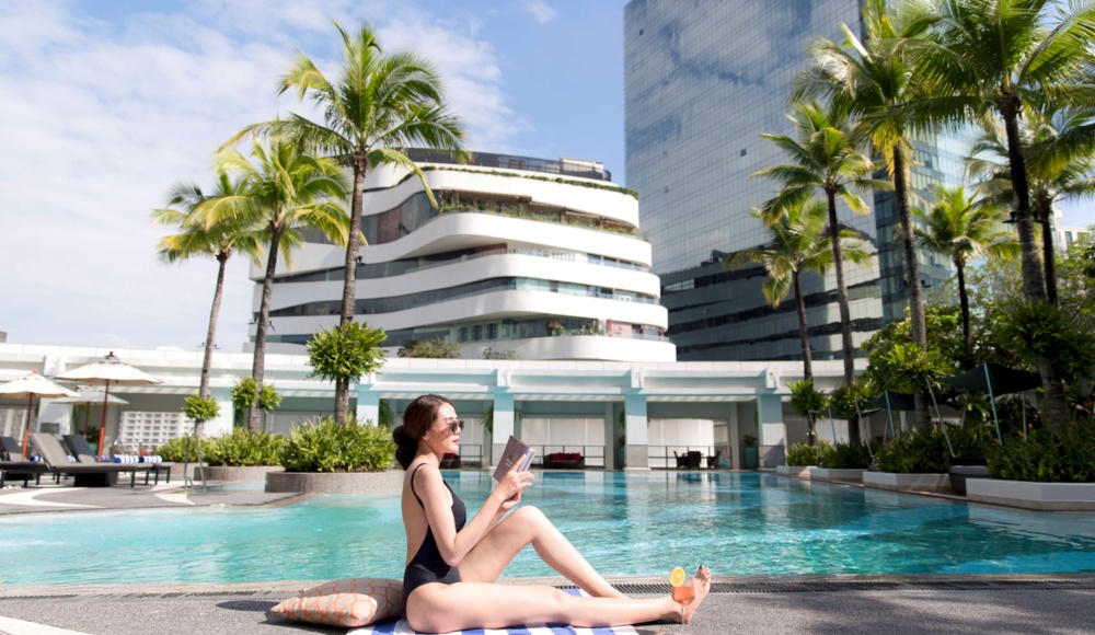 A woman in a bathing suit enjoys the sun while seated beside a tranquil swimming pool