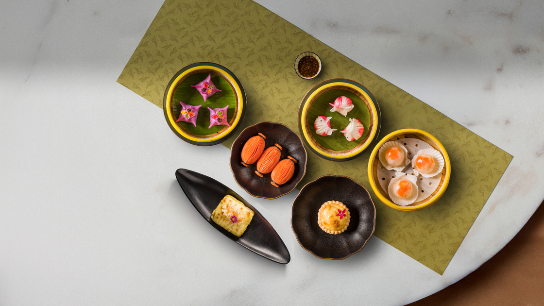 Assorted colorful dim sum and pastries on banana-leaf liners in bamboo steamers and ceramic dishes on a green placemat