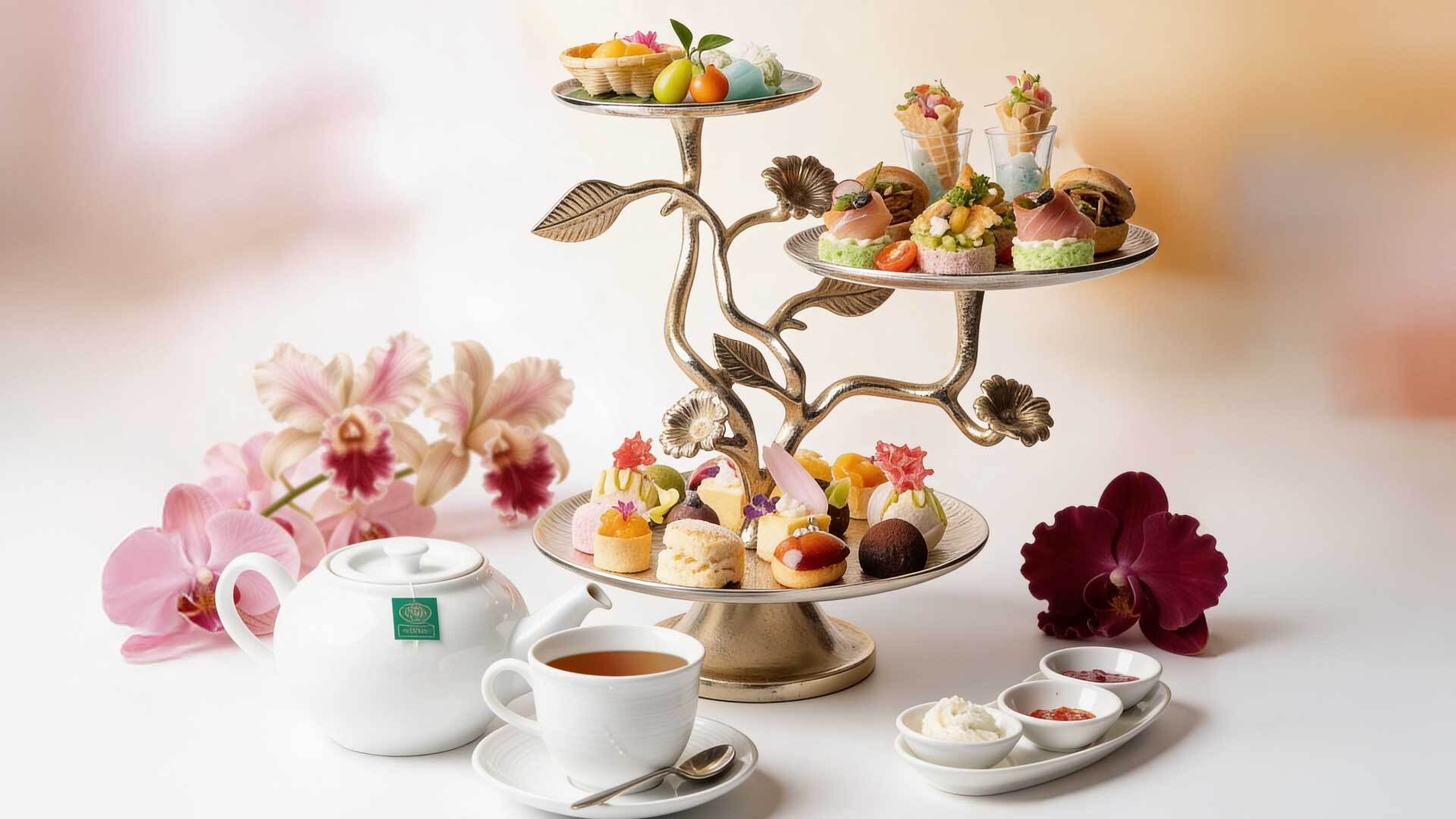 Three-tiered silver stand of pastries and savory canapés, white teapot and teacup, jam, clotted cream and pink orchids