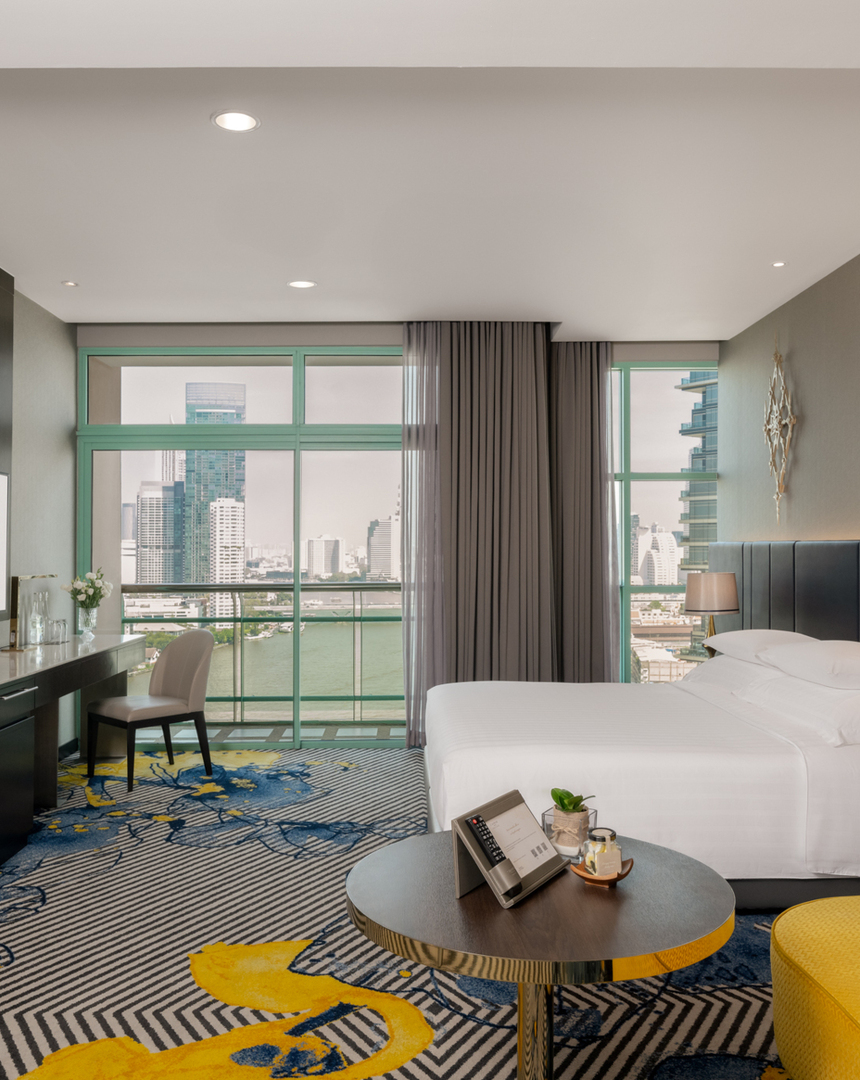 Riverside king room with floor-to-ceiling windows, balcony overlooking city skyline, yellow lounge and work desk