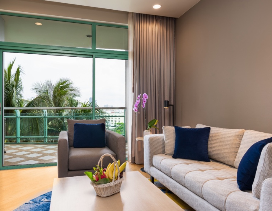 Bright suite living area with sofa and armchair, navy cushions, coffee table with fruit basket and orchid, balcony with palm view