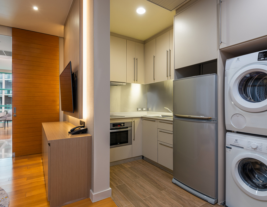 Modern studio kitchenette with full-size fridge, oven, stacked washer-dryer, sink and cabinets; wood sliding door and TV desk.