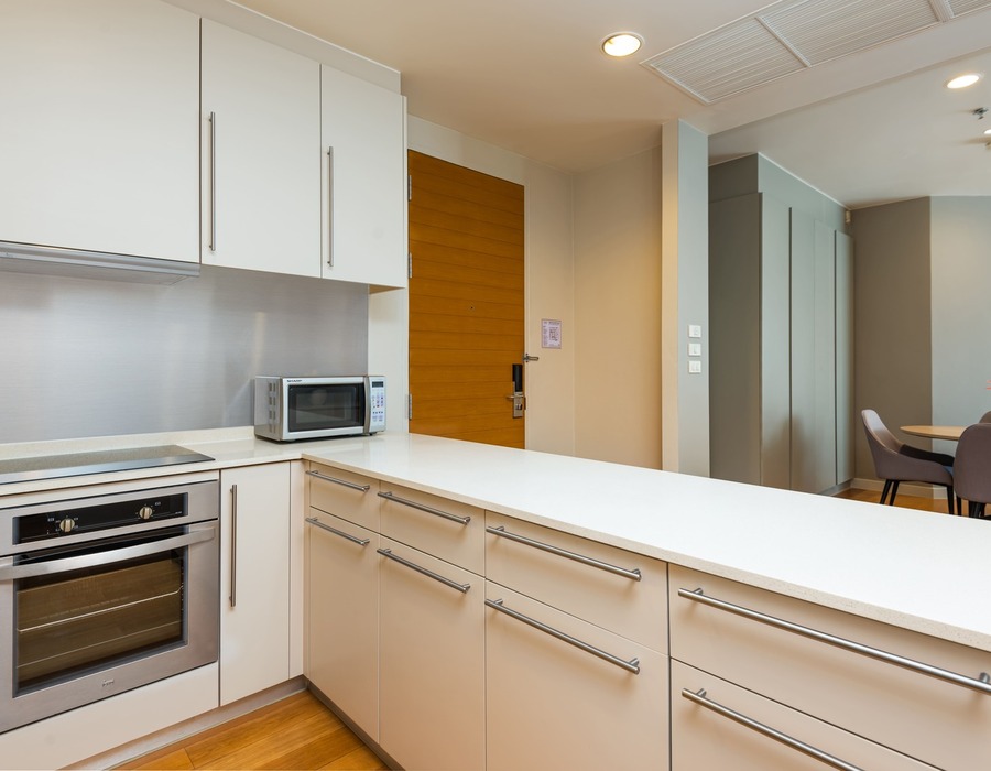 Modern suite kitchenette with white quartz counter, stainless oven and microwave, ample cabinets, dining nook with vase.