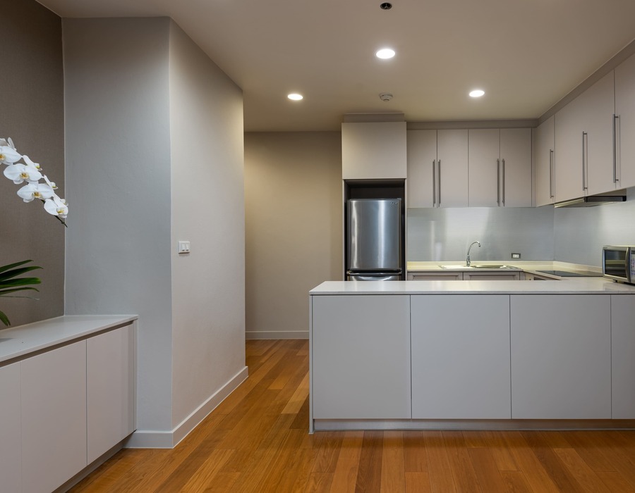 Modern hotel kitchenette with white island, stainless fridge, microwave, sink, ample cabinets, hardwood floors and white orchid.