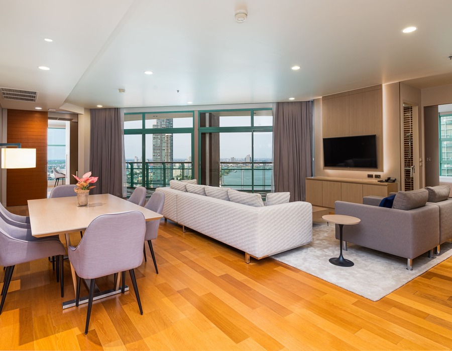 Spacious modern suite living/dining with hardwood floors, sofas, TV and balcony overlooking river and city skyline.