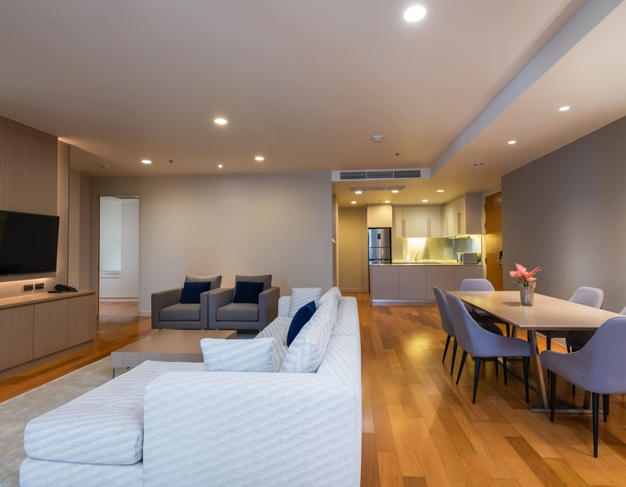 Open-plan suite with kitchenette, dining table, comfortable sofa and armchairs, wall TV, vase of flowers and wood floors.