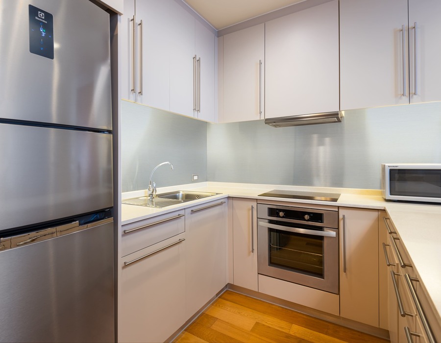 Suite kitchenette with stainless-steel fridge, oven, microwave, induction cooktop, sink, white cabinets and quartz counters.