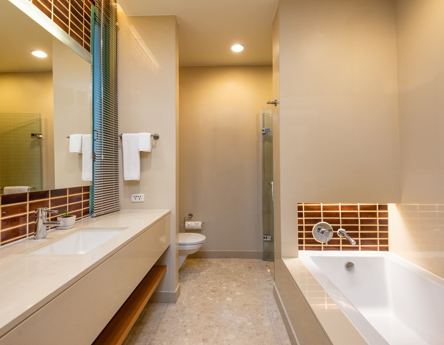 Spa‑style hotel bathroom with deep soaking tub, large vanity and mirror, glass shower, marble floor and warm accent tiles
