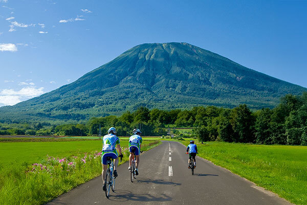 3人のサイクリストが山の背景を楽しみながら道を走り、アウトドアの冒険を満喫しています。