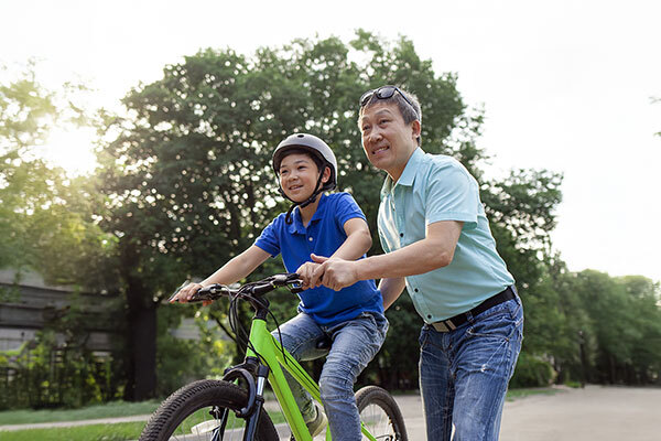 父と息子が緑の木々に囲まれた晴れた公園で楽しそうに一緒に自転車に乗っています。