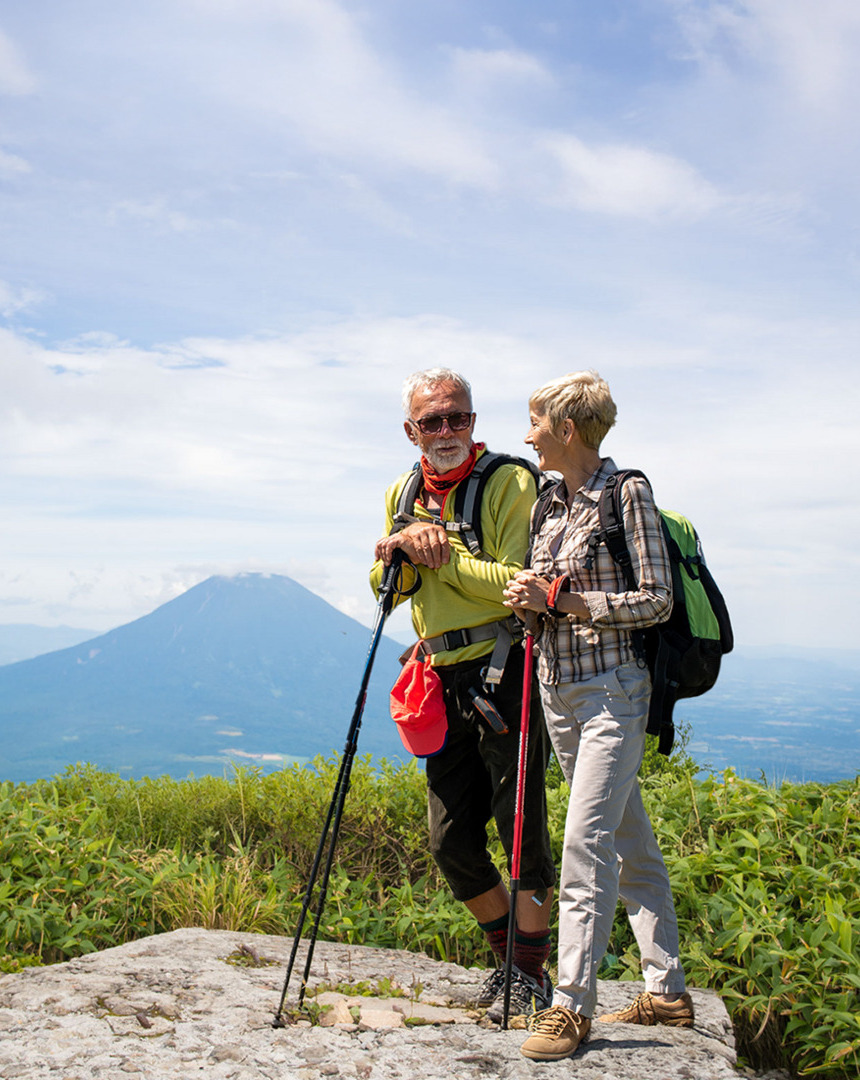 A man and woman hiking together on a scenic trail surrounded by trees and mountains.