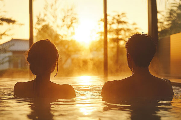 A couple relaxes in a onsen, basking in the warm glow of a sunset.