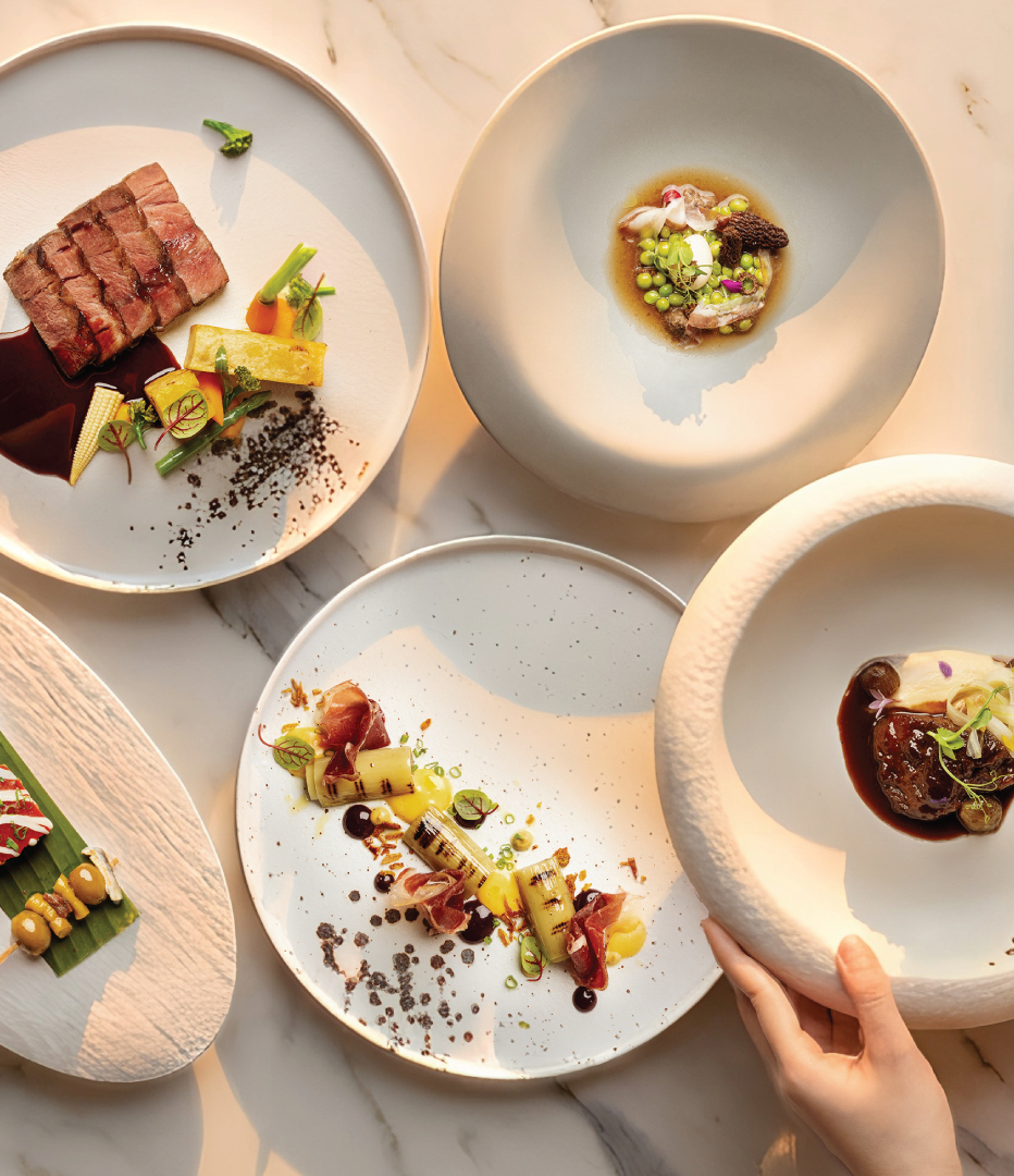 Fine-dining tasting menu: five artfully plated dishes on marble tabletop, steak and vegetable courses, hands placing bowl.