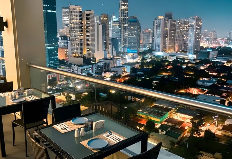 Rooftop terrace dining with glass railing, set tables for two and panoramic illuminated city skyline at night.