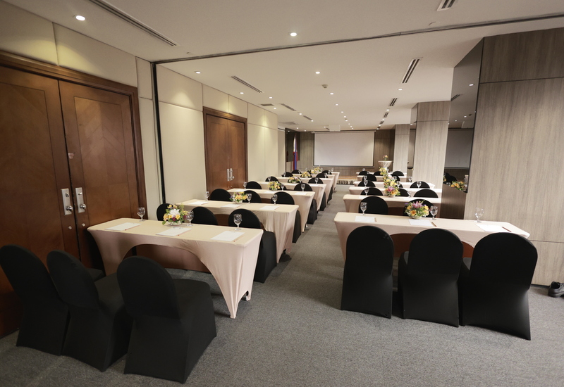 Conference room in classroom style with covered chairs, draped tables, floral centerpieces, water glasses and projection screen.