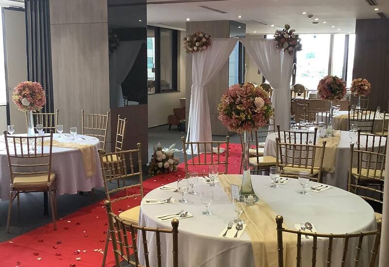 Elegant wedding reception room with round tables, white linen, gold Chiavari chairs, pink floral centerpieces and red carpet aisle