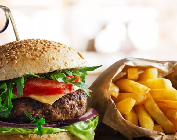 Gourmet sesame-bun burger with beef patty, cheese, tomato, arugula and red onion, served with a paper bag of golden fries