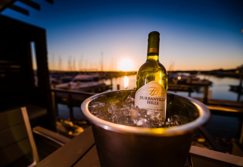 Chilled Durbanville Hills Sauvignon Blanc in an ice bucket on a marina terrace table at sunset, yachts and calm water beyond