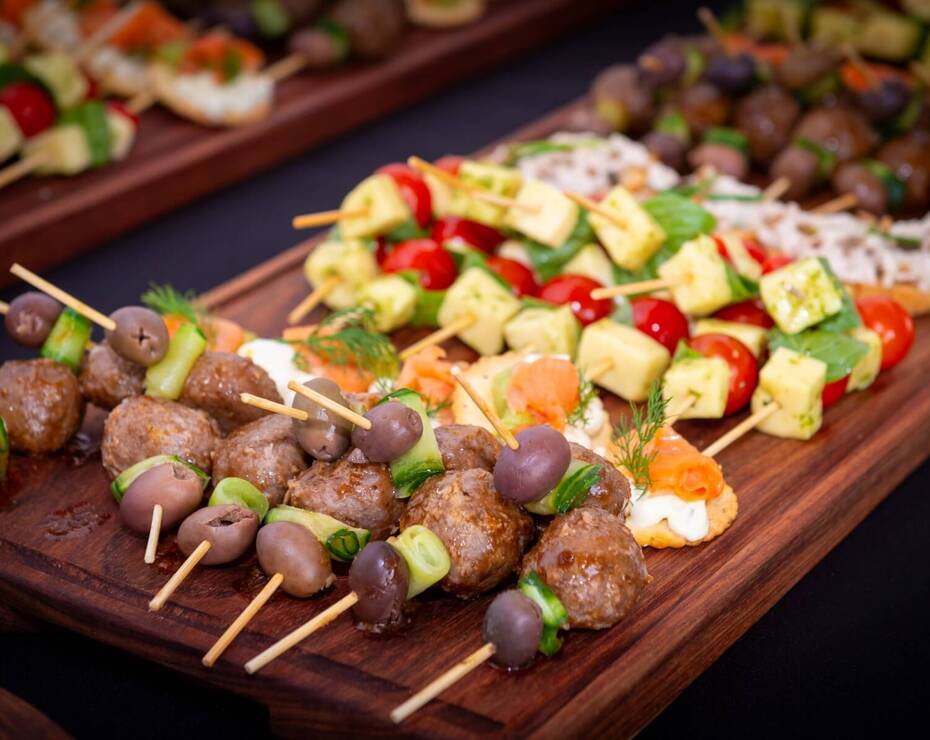 Assorted catering skewers on wooden board: glazed meatballs, olives & cucumber, tomato-cheese kebabs and smoked-salmon bites