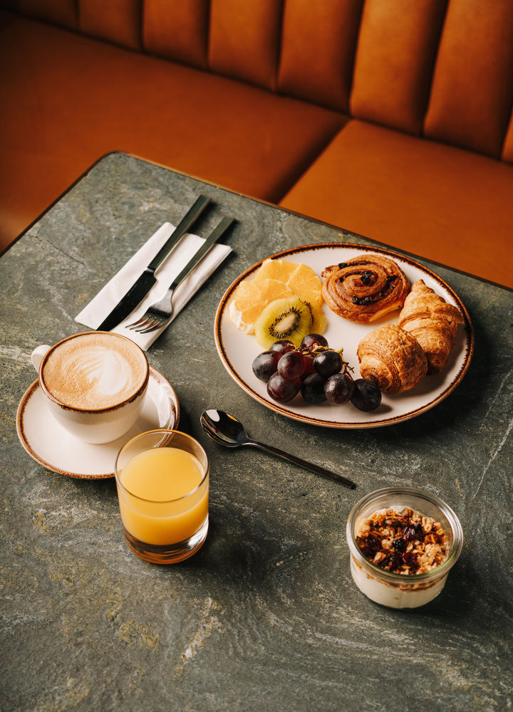 Sweet hotel breakfast on a plate with cutlery, coffee, juice, and yogurt with fruit