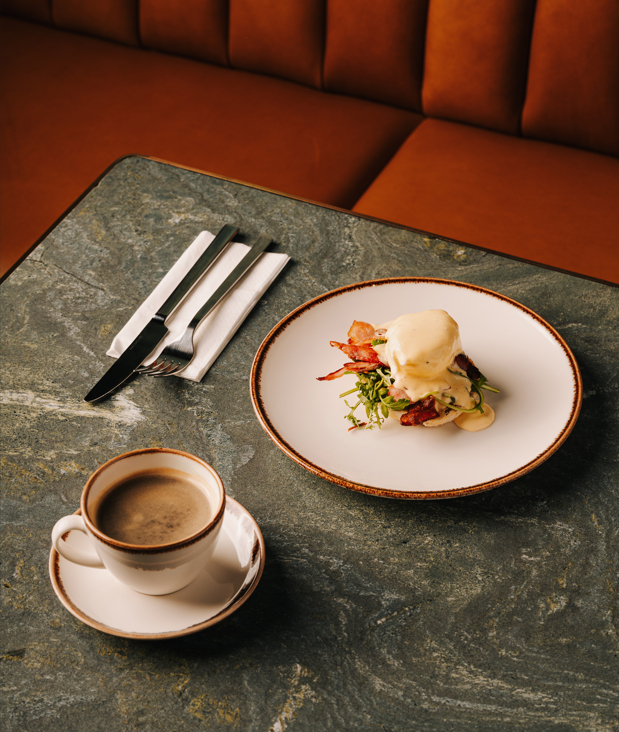 Frühstücksgericht Eggs Benedict mit pochiertem Ei, knusprigem Speck und Sauce Hollandaise auf einem Teller im eleganten Restaurant des Hotels The Cyrus – einem Fünf-Sterne-Hotel im Zentrum von Wrocław.