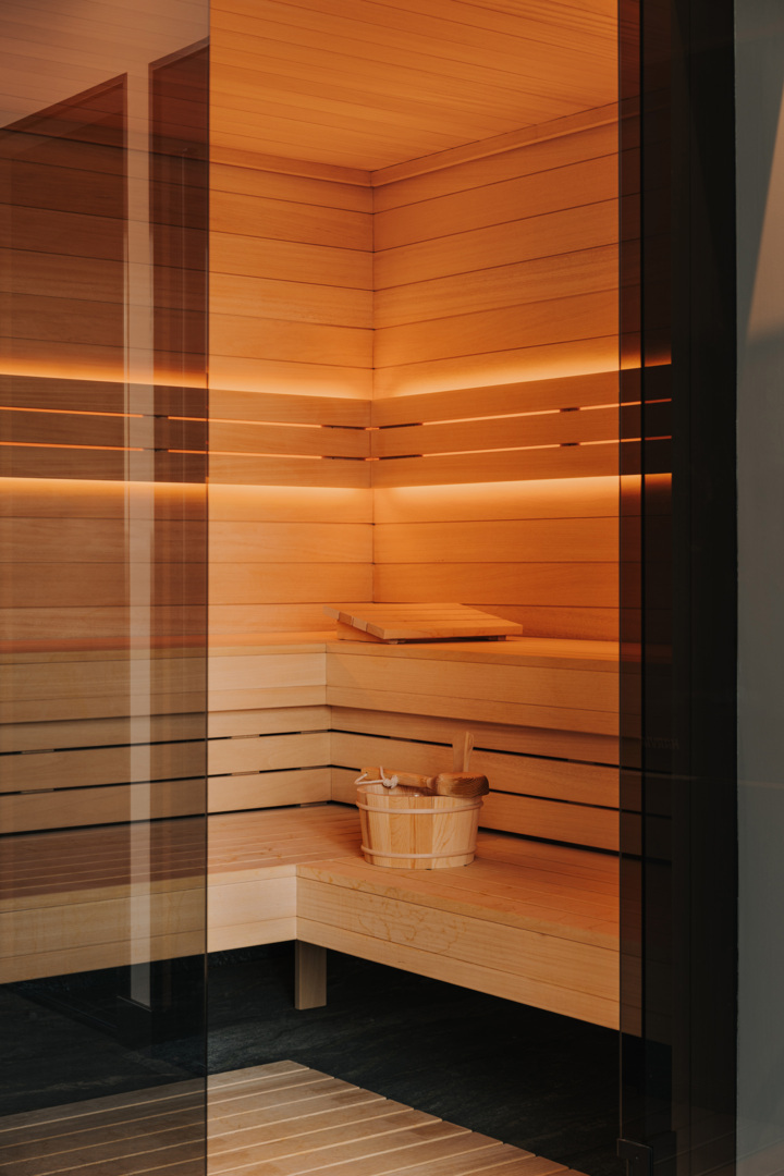 Moderne Hotelsauna mit hellem Holz, warmer Beleuchtung und einem Holzeimer mit Kelle für die Entspannung der Gäste.