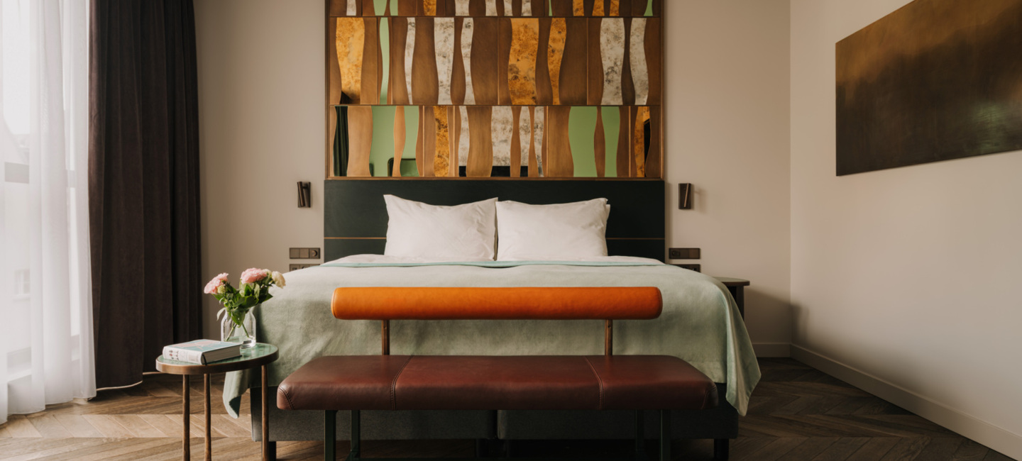 Nowoczesny pokój hotelowy z dużym łóżkiem, oryginalnym drewnianym zagłówkiem i elegancką ławką na drewnianej podłodze