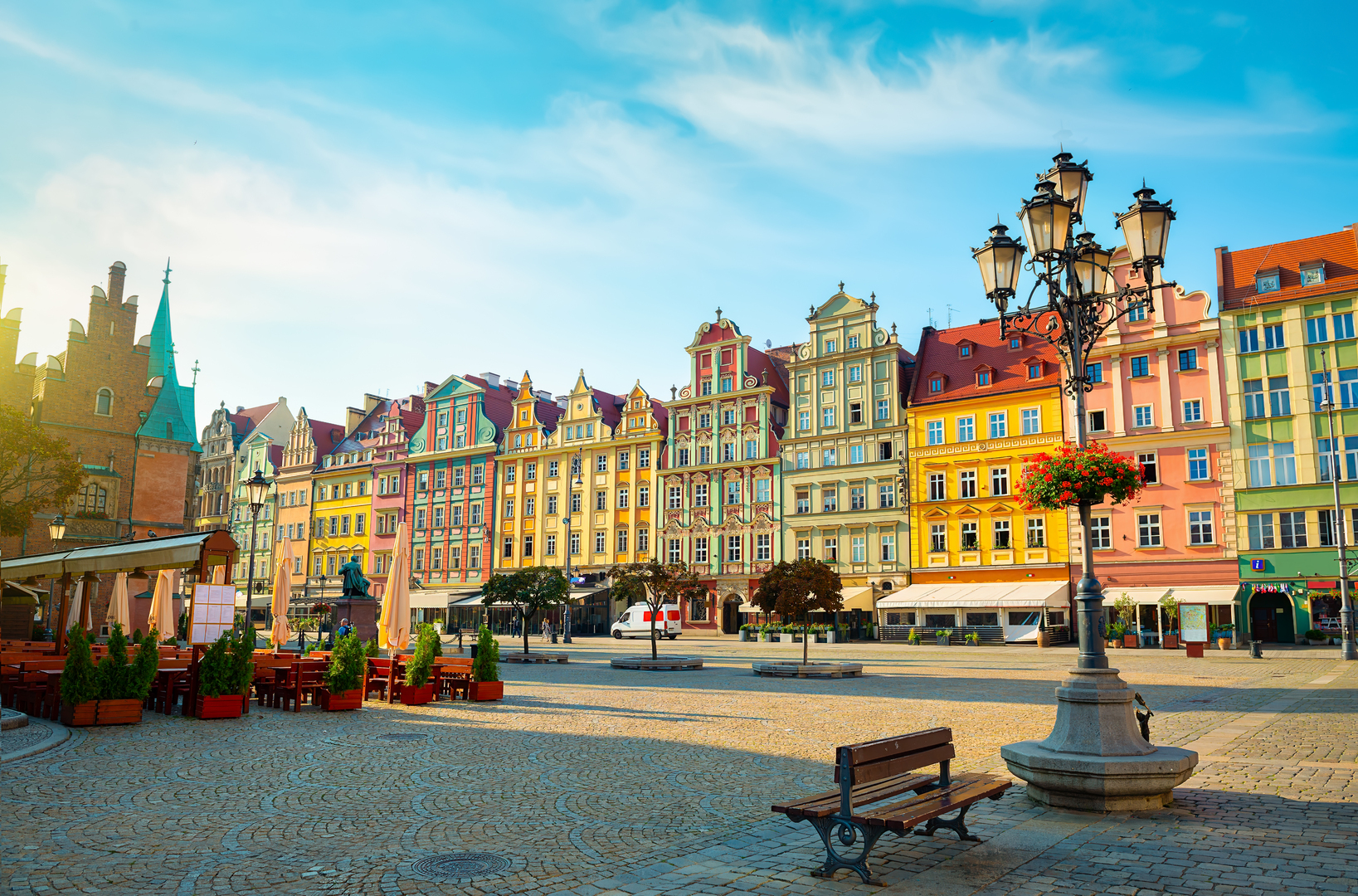 Bunte Bürgerhäuser am Breslauer Marktplatz, pastellfarbene Fassaden historischer Gebäude, gepflasterter Platz mit Bänken und Straßenlaternen an einem sonnigen Tag, zentrale Lage im Herzen von Breslau.