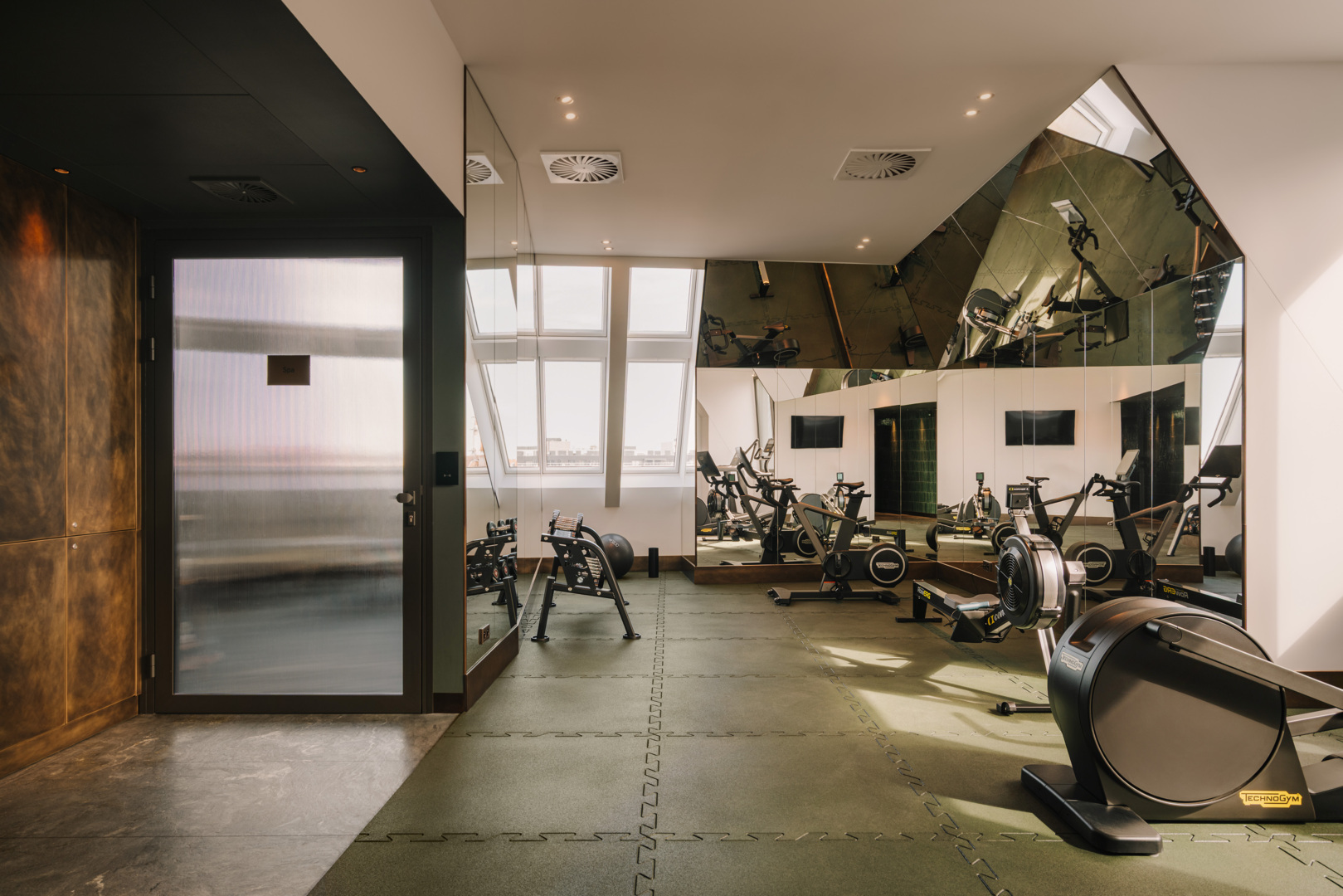Modern hotel gym with stationary bikes, mirrored walls, and frosted door leading to spa area