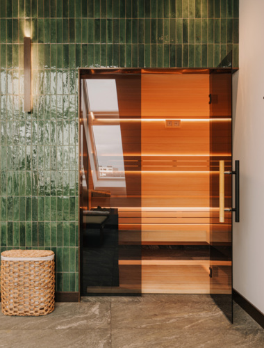 Moderner Wellnessbereich mit Holzinneinrichtung der Sauna, Glastüren, grüner Fliesenwand und Steinboden im Hotel In einem Hotel mit Spa im Zentrum von Breslau.
