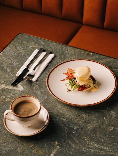 Frühstücksgericht Eggs Benedict mit pochiertem Ei, knusprigem Speck und Sauce Hollandaise auf einem Teller im eleganten Restaurant des Hotels The Cyrus – einem Fünf-Sterne-Hotel im Zentrum von Wrocław.