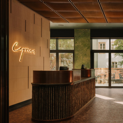 Elegancka recepcja The Cyrus Hotel Wrocław wykończona naturalnymi materiałami - brązem i kamieniem, z ciemną drewnianą podłogą i widokiem na patio przez duże okna.