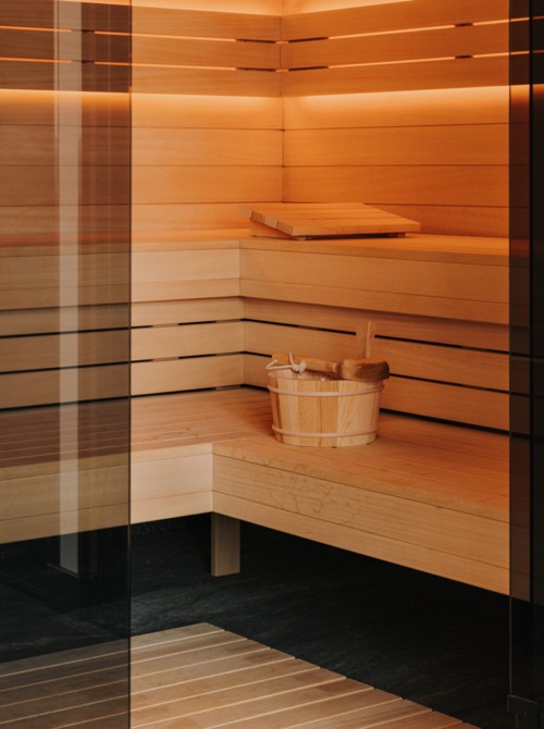 Nowoczesna sauna hotelowa z drewnianymi ławami, delikatnym podświetleniem i drewnianym wiadrem z chochlą.