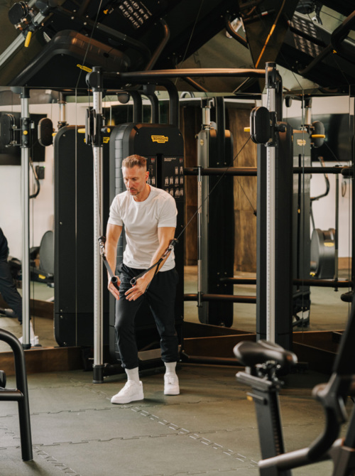 Gość trenuje na maszynie do ćwiczeń siłowych w nowoczesnej siłowni hotelowej z lustrzaną ścianą.