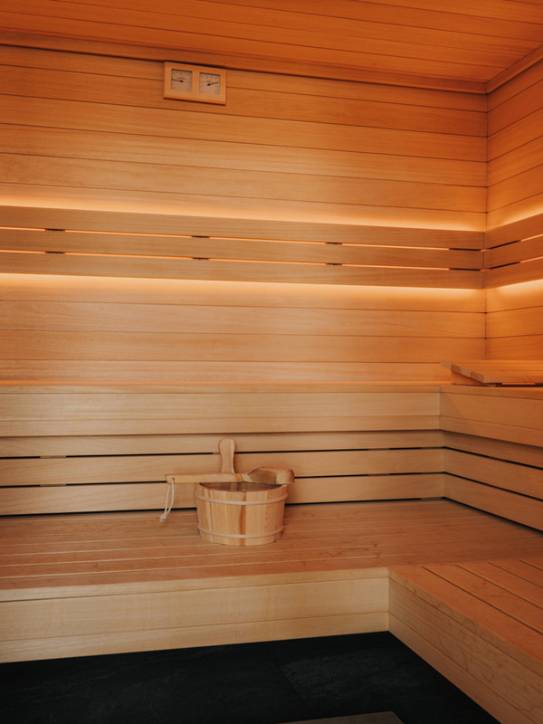 Przytulna sauna hotelowa z jasnego drewna, podświetlanymi panelami i drewnianą wiadrem do wody dla relaksu.