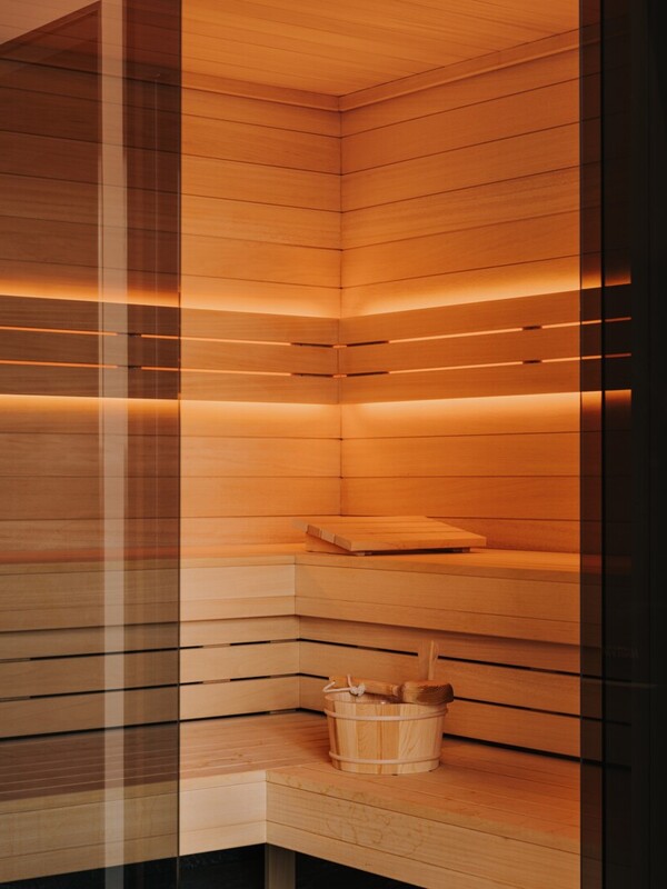 Moderne Hotel-Sauna mit hellen Holzwänden, sanfter Hintergrundbeleuchtung und Holzeimer mit Kelle zur Entspannung der Gäste