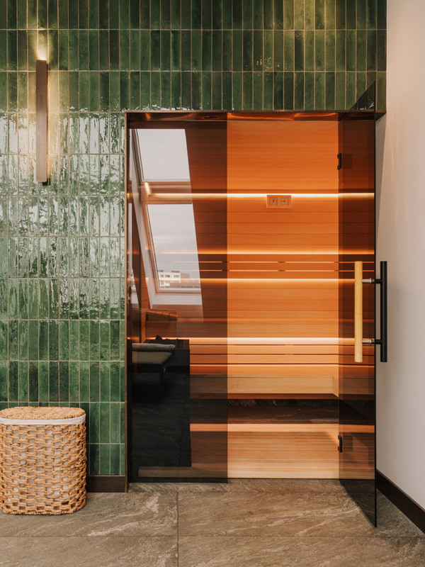 Nowoczesna sauna z drewnianym wnętrzem, szklanymi drzwiami i zieloną, płytkową ścianą w strefie spa w hotelu ze spa w centrum Wrocławia