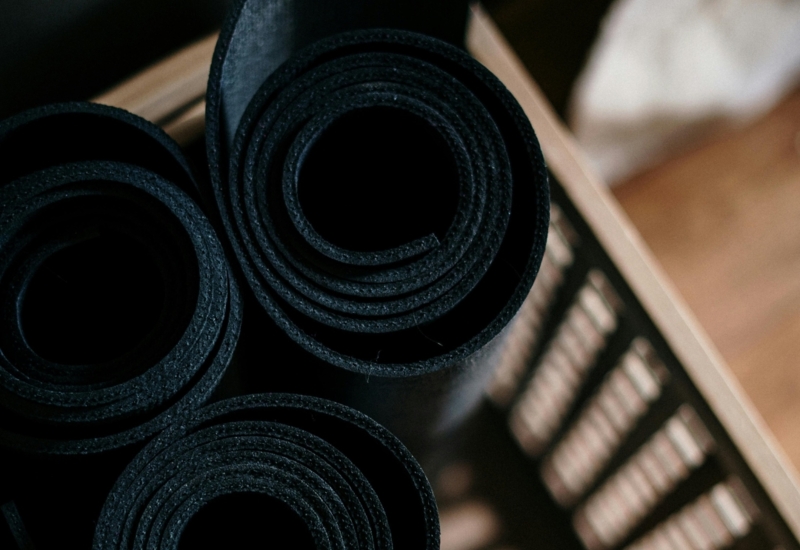 Zrolowane czarne maty do jogi umieszczone w drewnianym koszu, gotowe do ćwiczeń w hotelowej siłowni lub spa