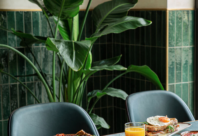 Wykwintne śniadanie hotelowe z jajkiem sadzonym, kiełbaskami, warzywami, sokiem pomarańczowym i zielonym roślinem w tle