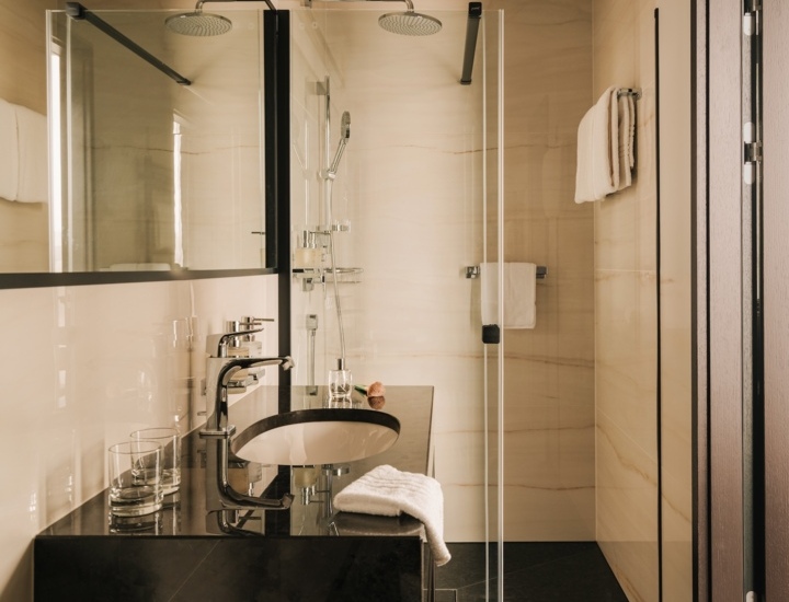 Nowoczesna łazienka hotelowa z czarną umywalką, przestronnym prysznicem z deszczownicą i eleganckim marmurowym wnętrzem