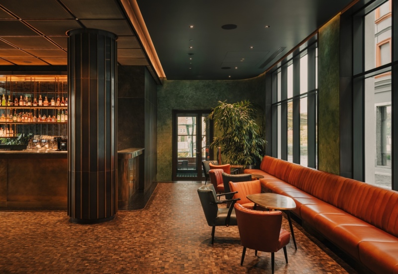 Elegancki hotelowy bar z brązową skórzaną sofą, wygodnymi fotelami i dużymi oknami przy ulicy