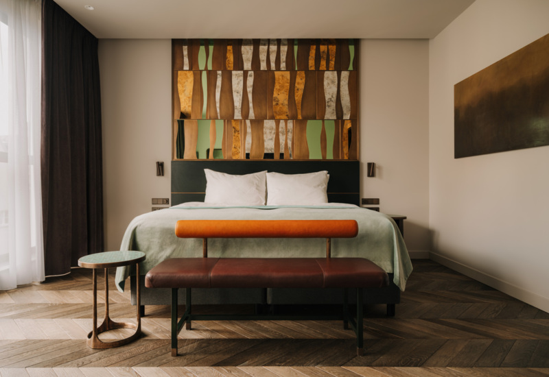 Nowoczesny pokój hotelowy z dużym łóżkiem, ozdobną drewnianą ścianą nad głową i elegancką ławką u stóp łóżka