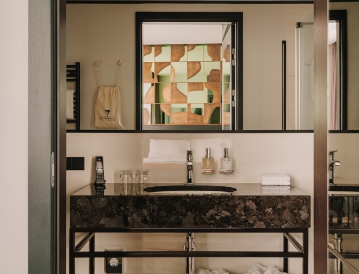 Nowoczesna łazienka hotelowa z czarnym kamiennym blatem, lustrem, dwoma szklankami, szlafrokami i ręcznikami.