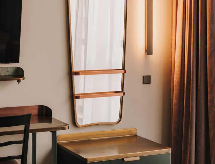 Stylowa toaletka z dużym lustrem o zaokrąglonych narożnikach, mosiężną powierzchnią i zielonymi szufladami w eleganckim pokoju hotelowym.