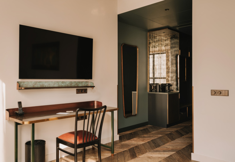 Nowoczesny hotelowy pokój z biurkiem, krzesłem z czerwonym siedziskiem, dużym telewizorem i komodą z ekspresem do kawy