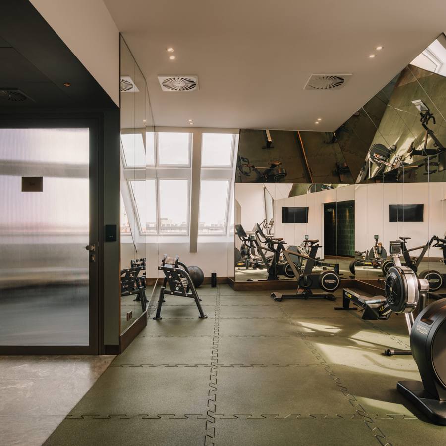 Nowoczesna siłownia hotelowa z rowerami stacjonarnymi, lustrzanymi ścianami i drzwiami do strefy spa