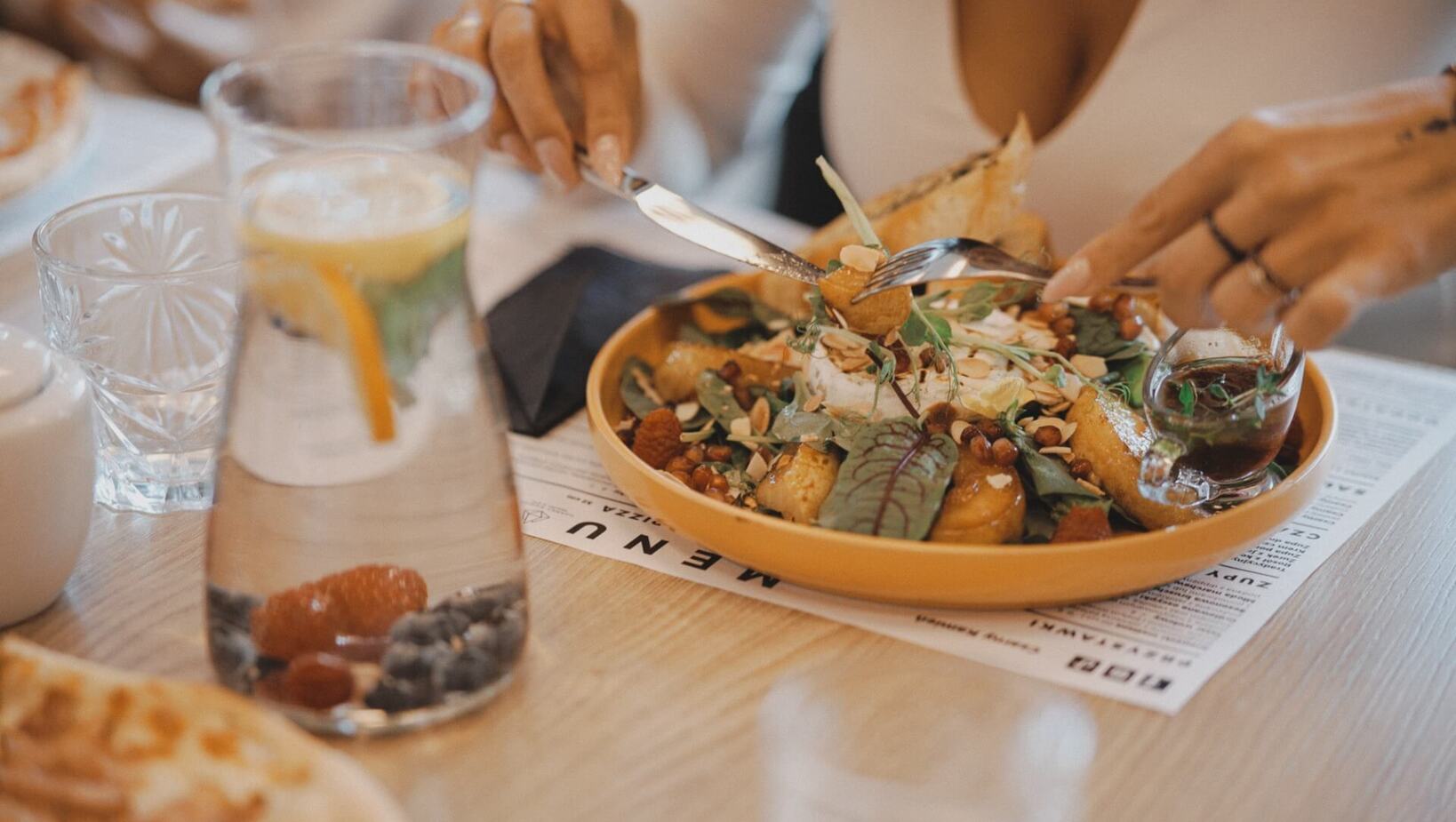 Gość kroi świeżą sałatkę z orzechami i listkami bazylii przy stole w restauracji hotelowej