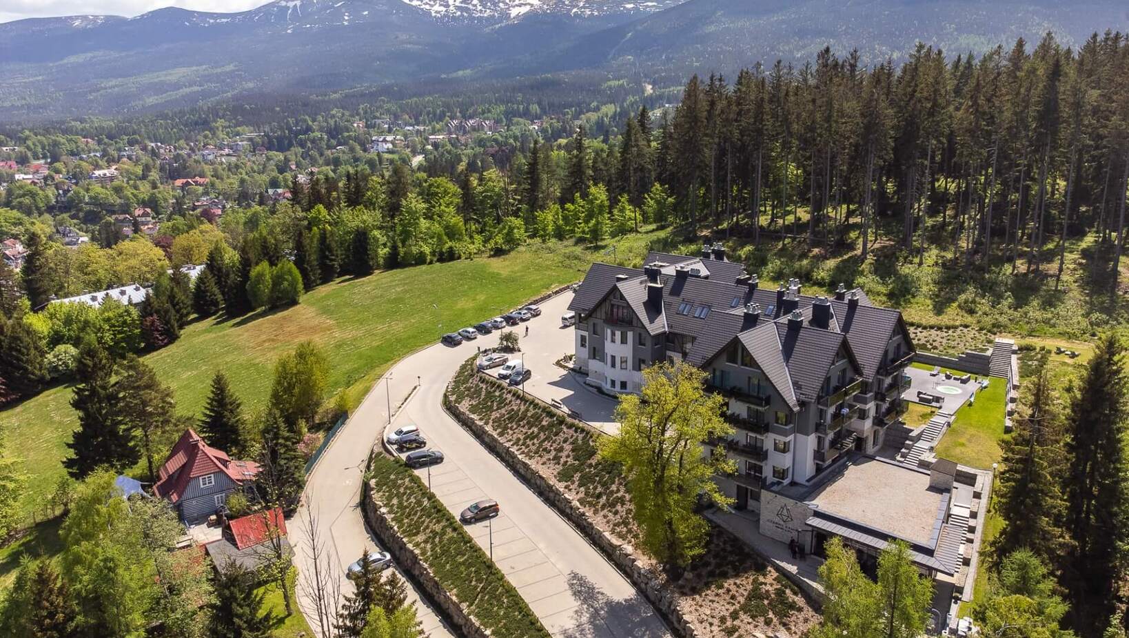 Nowoczesny hotel górski z tarasem i ogrodem, otoczony lasem, z widokiem na zalesione pasmo gór ze śniegiem.